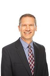 Paul Dybdahl stands in front of a white background. He smiles at the camera.